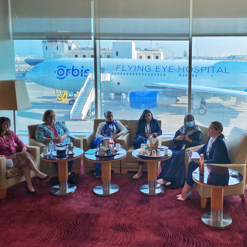 Group of women engaging in discussion at an airport with the Orbis Flying Eye Hospital in the background